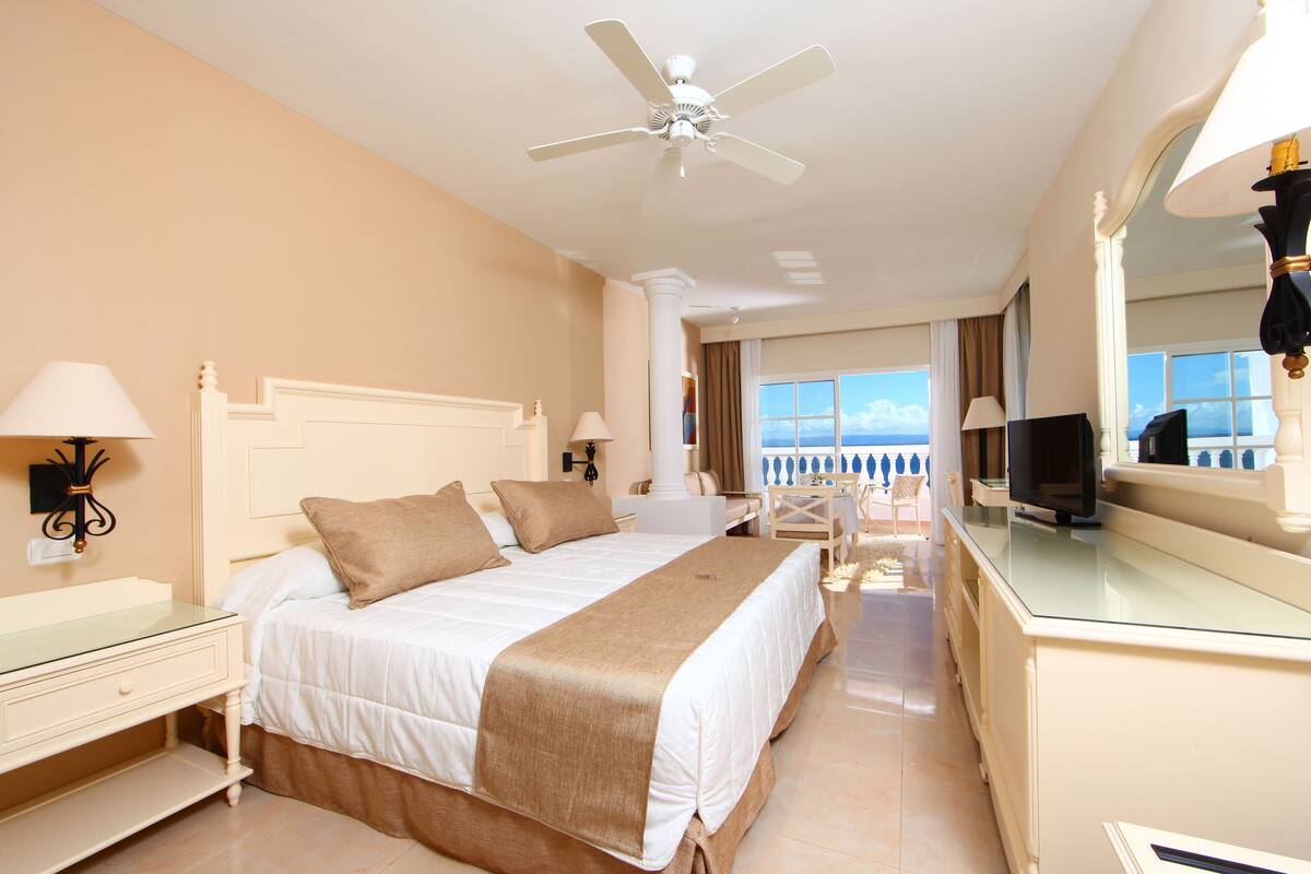 Une chambre d’hôtel avec un grand lit, un ventilateur de plafond, une télévision et une vue sur l’océan.