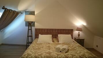 A hotel room with a bed, two pillows, a nightstand with a lamp, a floor lamp, and a window with curtains.