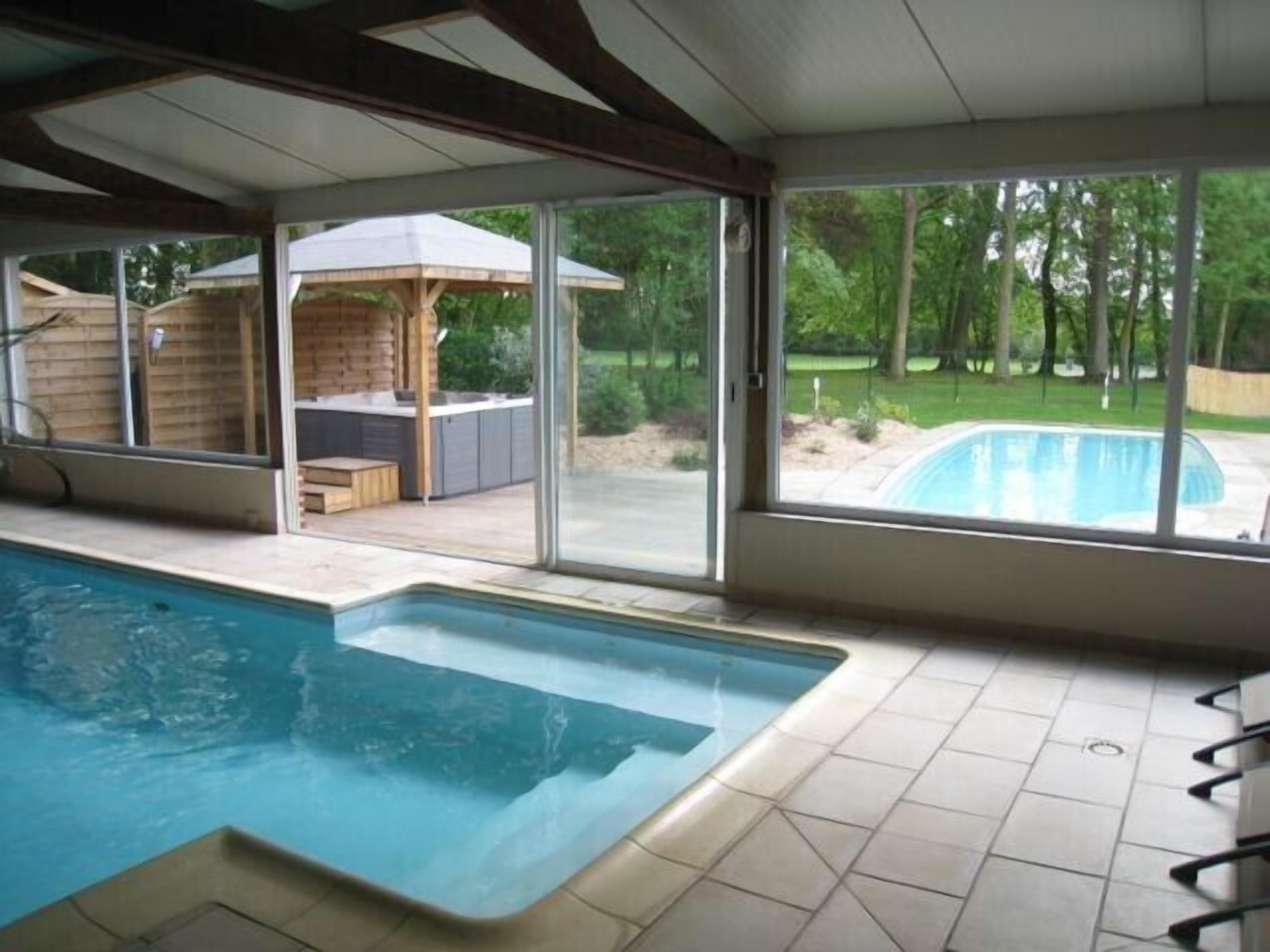 An indoor swimming pool with a view of a backyard and a covered patio area.