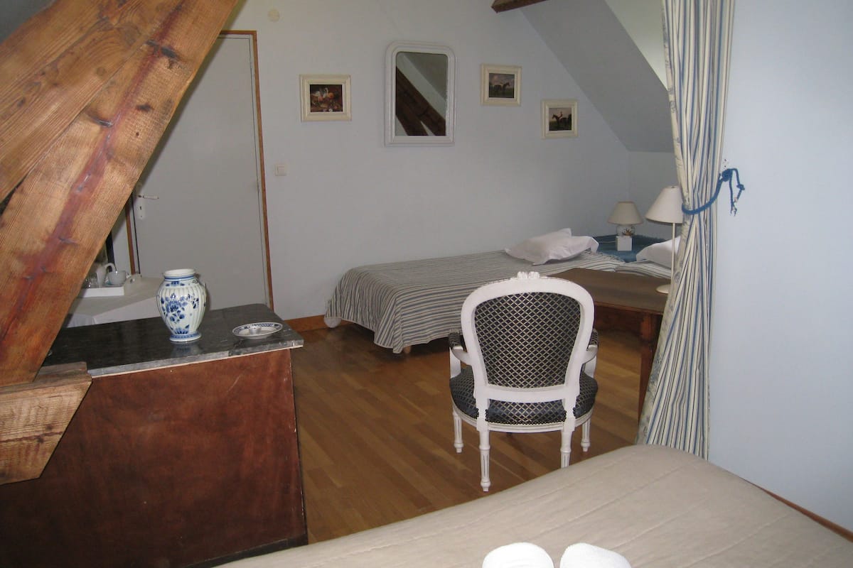 Une chambre à coucher avec un lit, une chaise, un bureau et une petite table sur laquelle se trouve un vase.