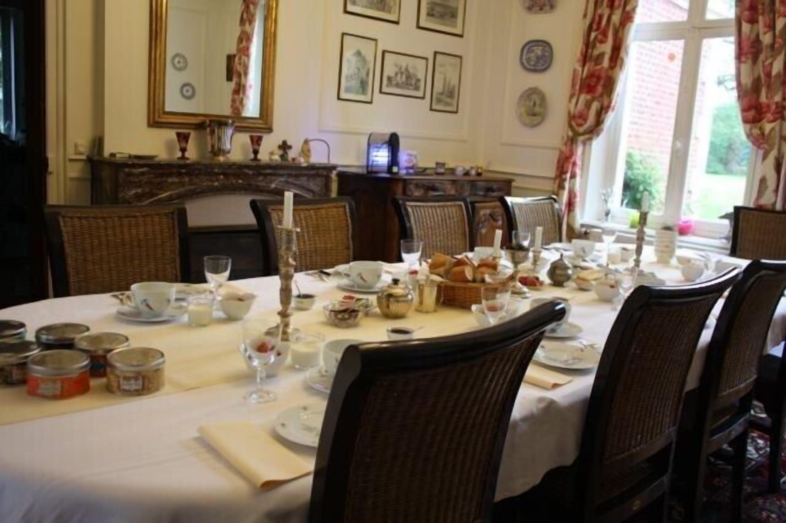 A dining room with a round table set for a meal, surrounded by wicker chairs.