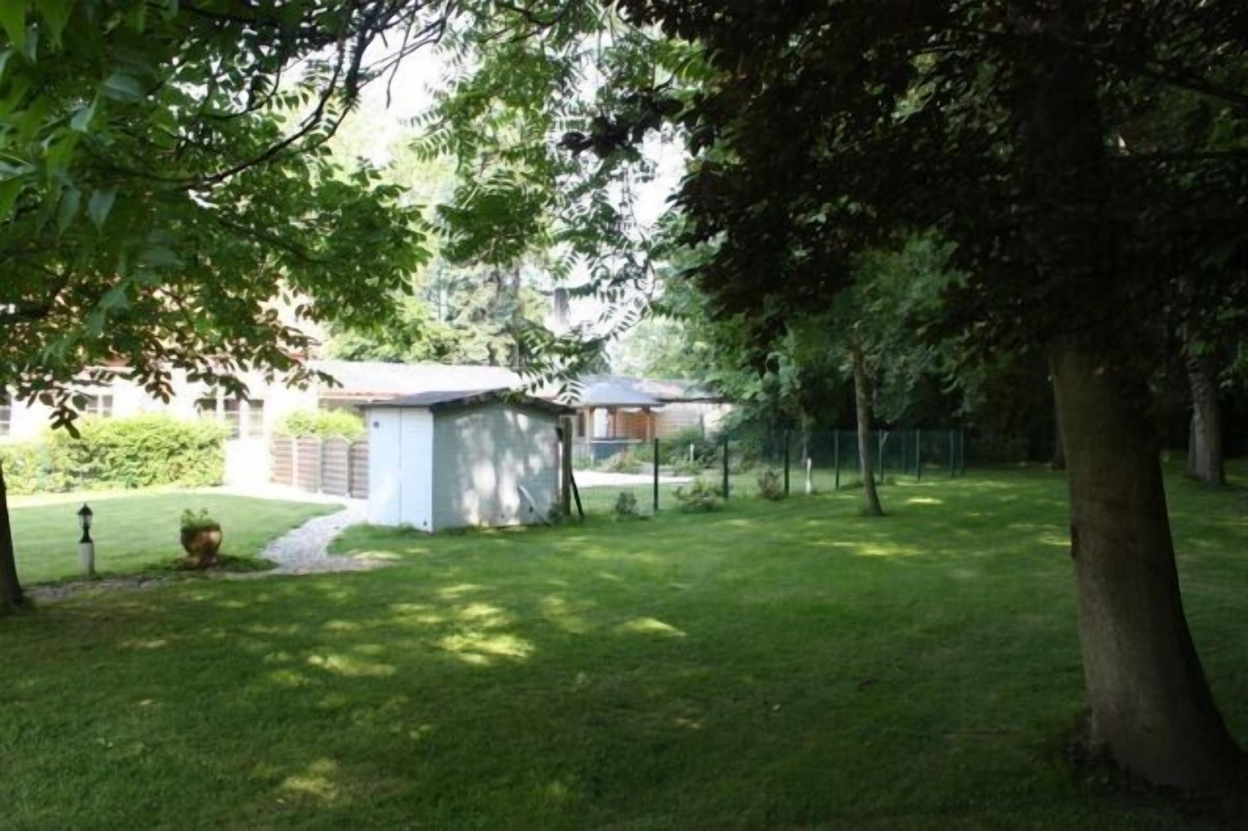 Ein gepflegter Garten mit einem kleinen Schuppen, einer Rasenfläche und Bäumen, die Schatten spenden.