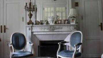 A room with a fireplace, two chairs, a small table, and a chandelier.