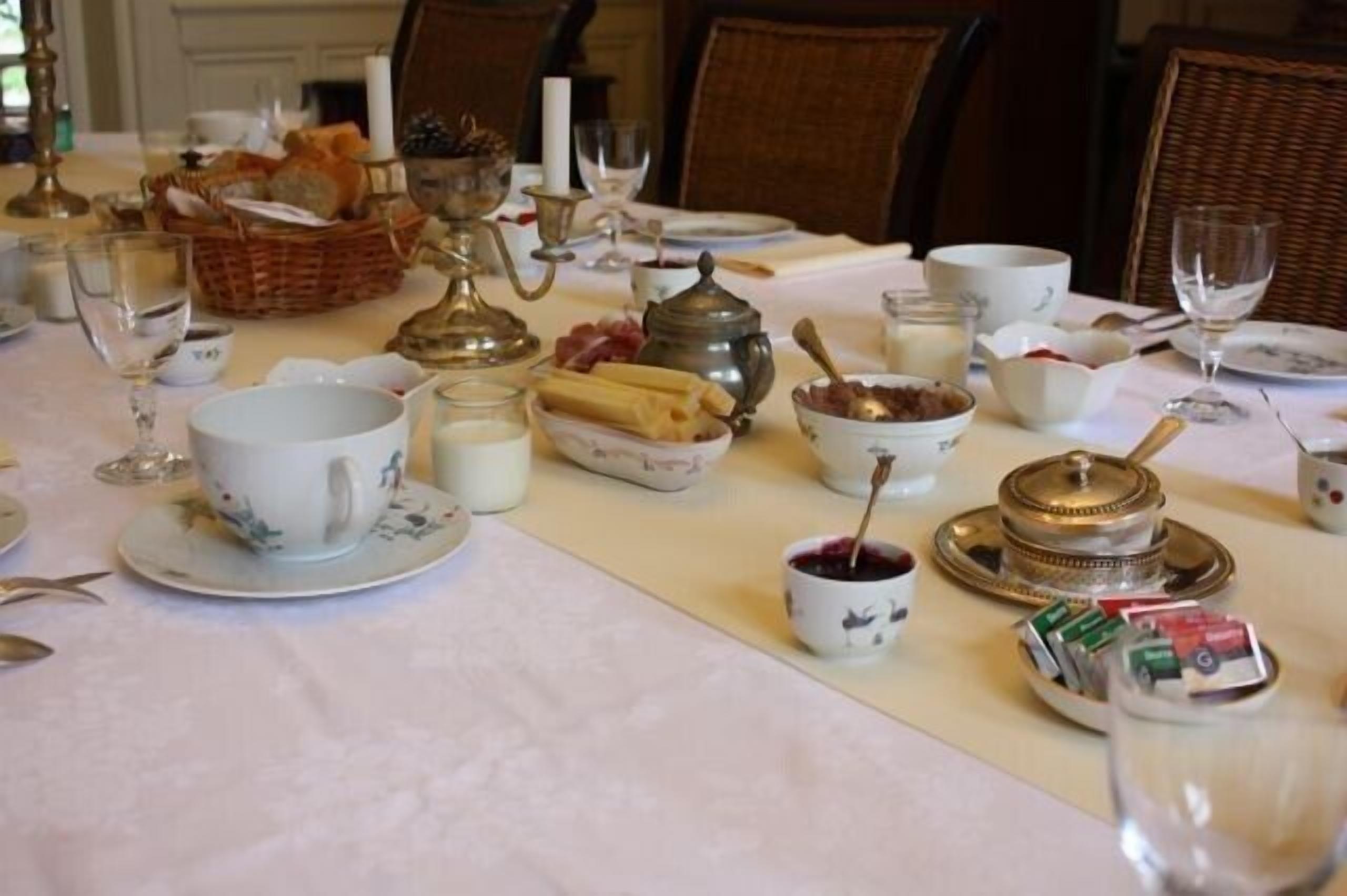 A dining table set with various dishes, including bread, cheese, and a teapot, suggesting a meal setting.