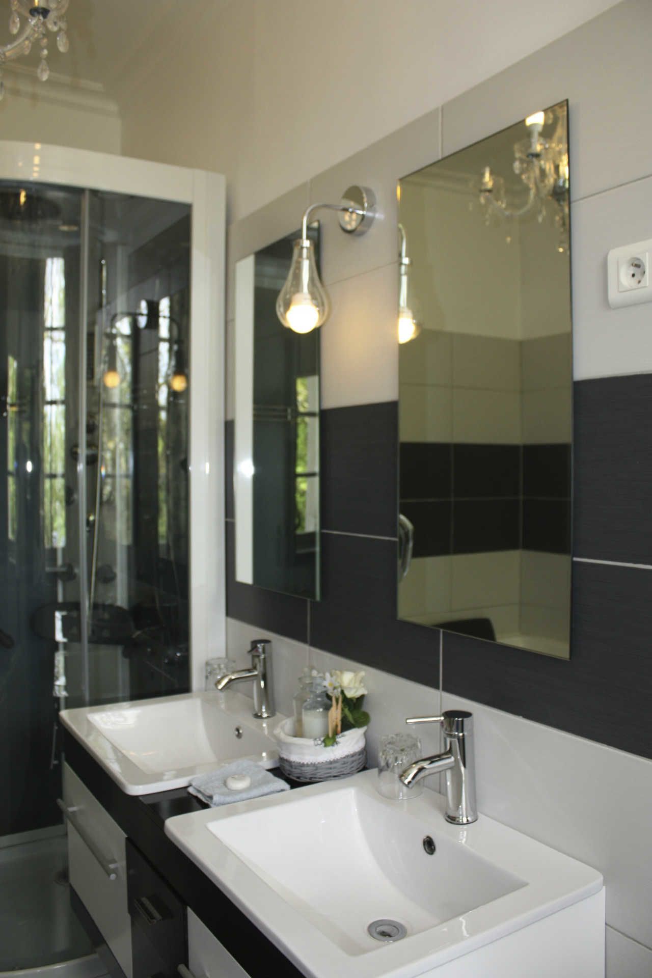 Une salle de bain moderne avec deux vasques blanches, un grand miroir et des luminaires suspendus.
