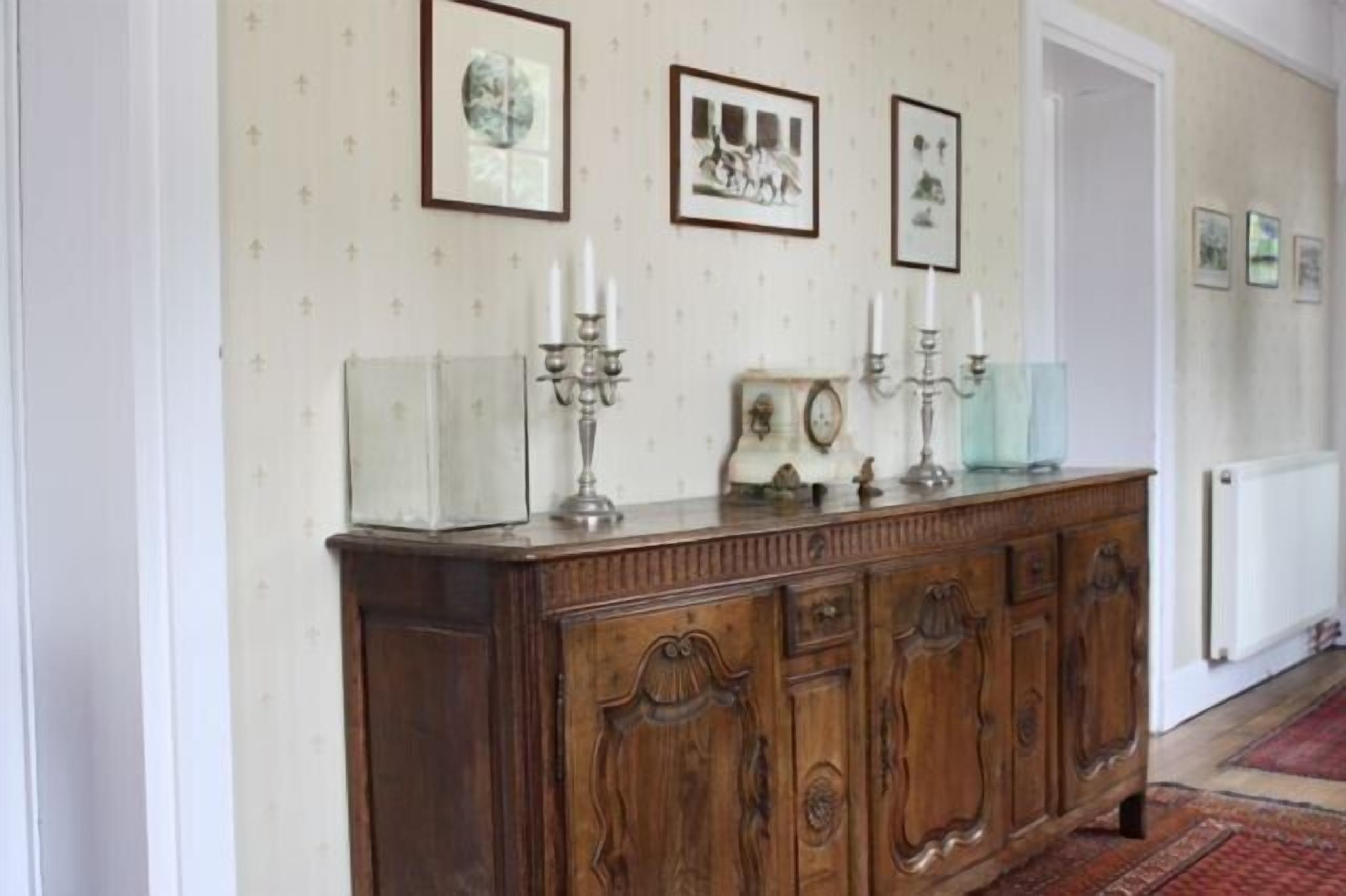 Een gang met een houten kast, kunstwerken in een lijst aan de muur en een radiator.
