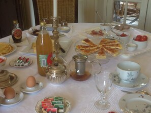 Ein Frühstückstisch reichhaltig gedeckt mit verschiedenen Speisen, darunter Pfannkuchen, Fruchtkonfitüre, Eier und einer Flasche Ahornsirup.