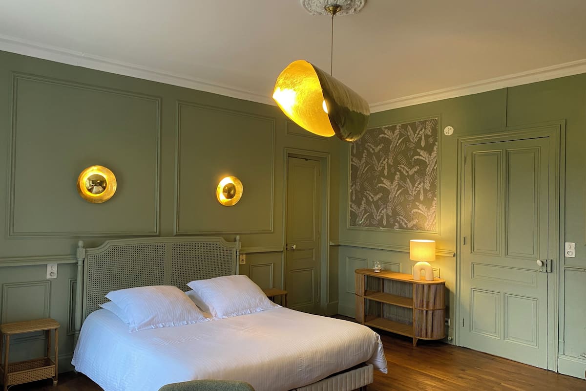 Une chambre à coucher bien aménagée, avec un grand lit, deux appliques murales, une table de chevet et un luminaire suspendu.