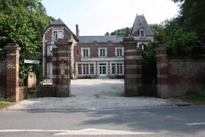 Un grand bâtiment historique à la façade symétrique, doté d’une entrée centrale et d’une allée bordée de portails.