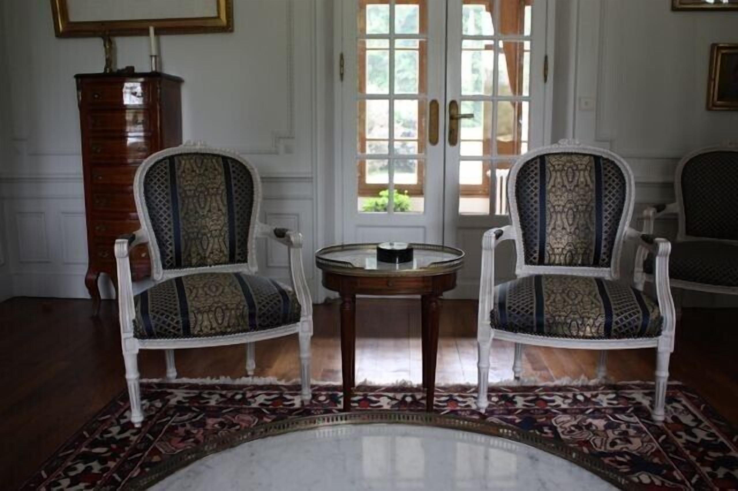 Ein Zimmer mit zwei verzierten Stühlen mit gemusterten Polstern, einem kleinen runden Tisch und einem Teppich mit Muster.