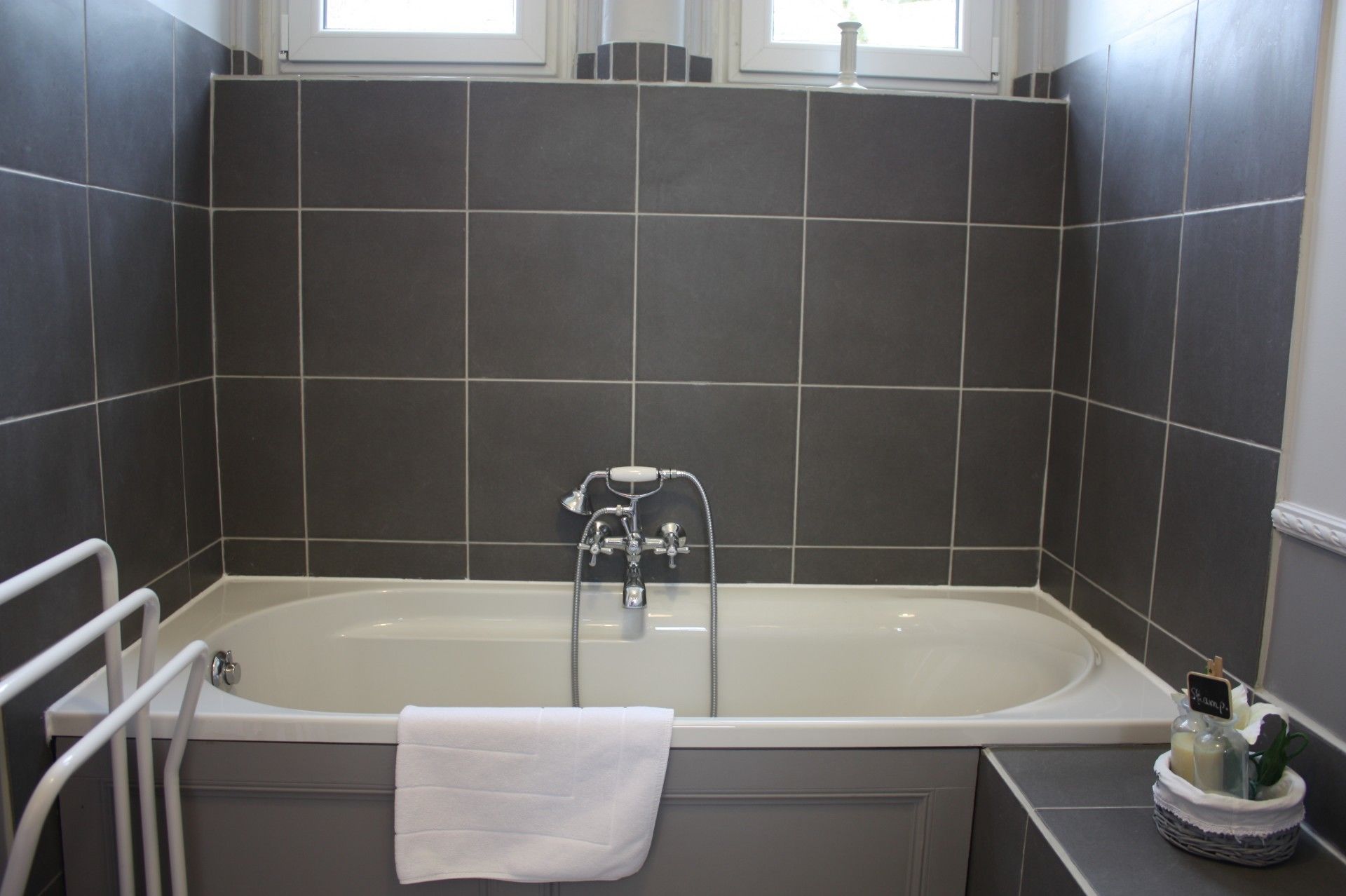 Une salle de bain moderne avec une baignoire sur pieds, une serviette blanche et un petit panier contenant des articles de toilette.