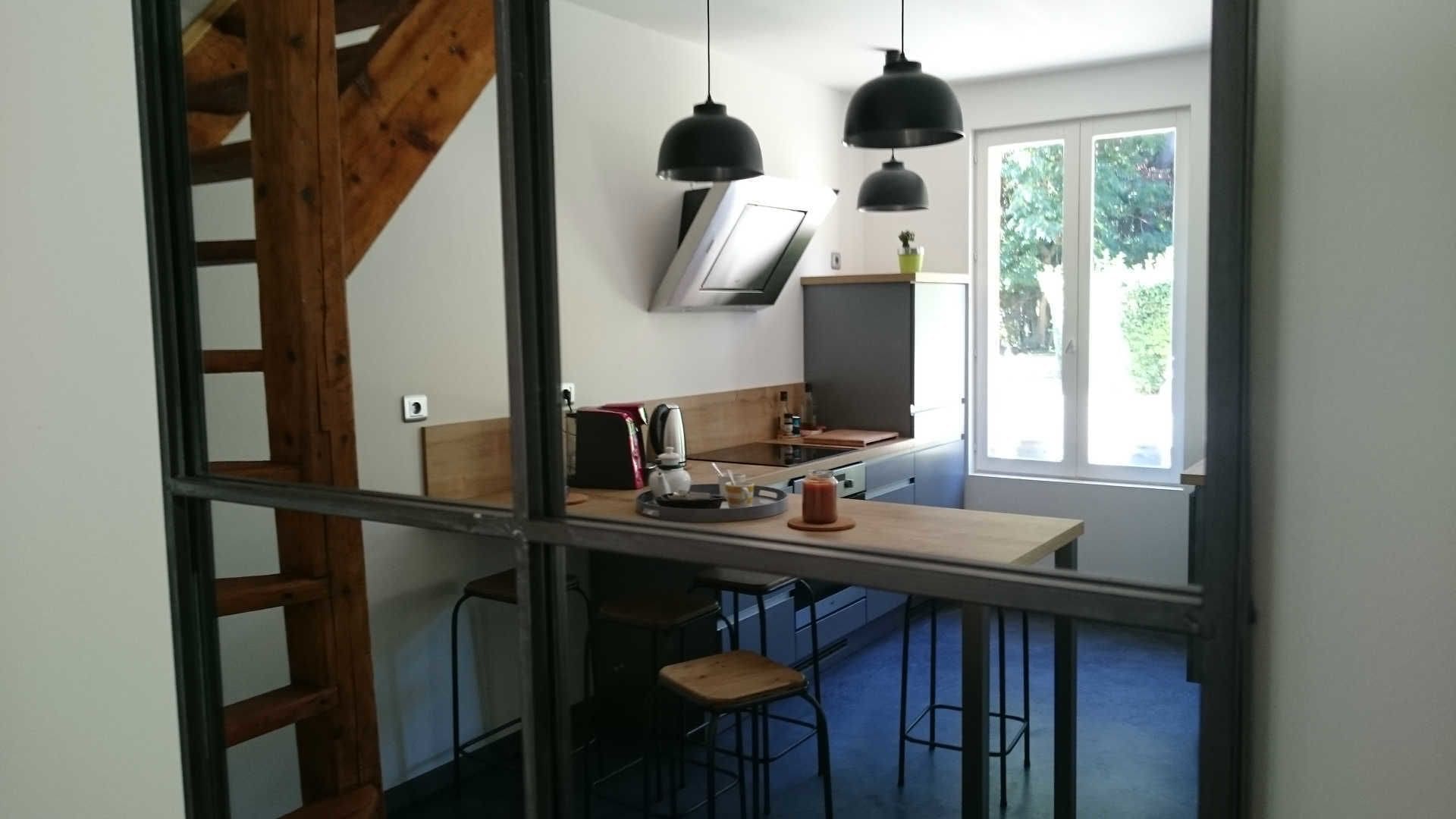A modern kitchen with a wooden staircase, a dining area with stools, and a large window providing natural light.