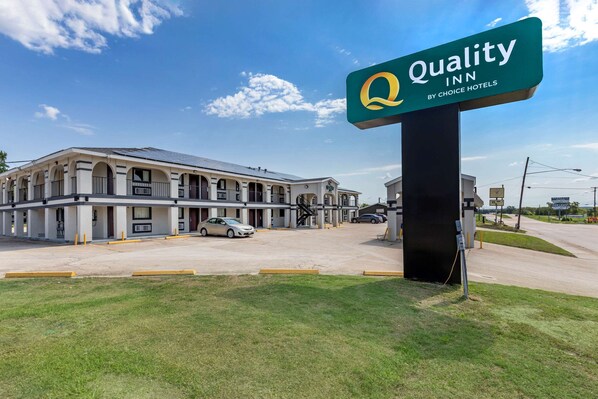 A Quality Inn by Choice Hotels with a large sign, a parking lot, and a building with multiple balconies.
