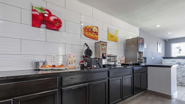 A modern kitchen with dark cabinetry, a large island, and a breakfast bar. There are fruit and waffle images on the wall, and a waffle maker on the counter. - Quality Inn Cameron (Cameron)
