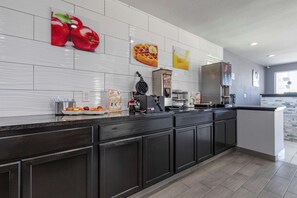 A modern kitchen with dark cabinetry, a large island, and a breakfast bar. There are fruit and waffle images on the wall, and a waffle maker on the counter.