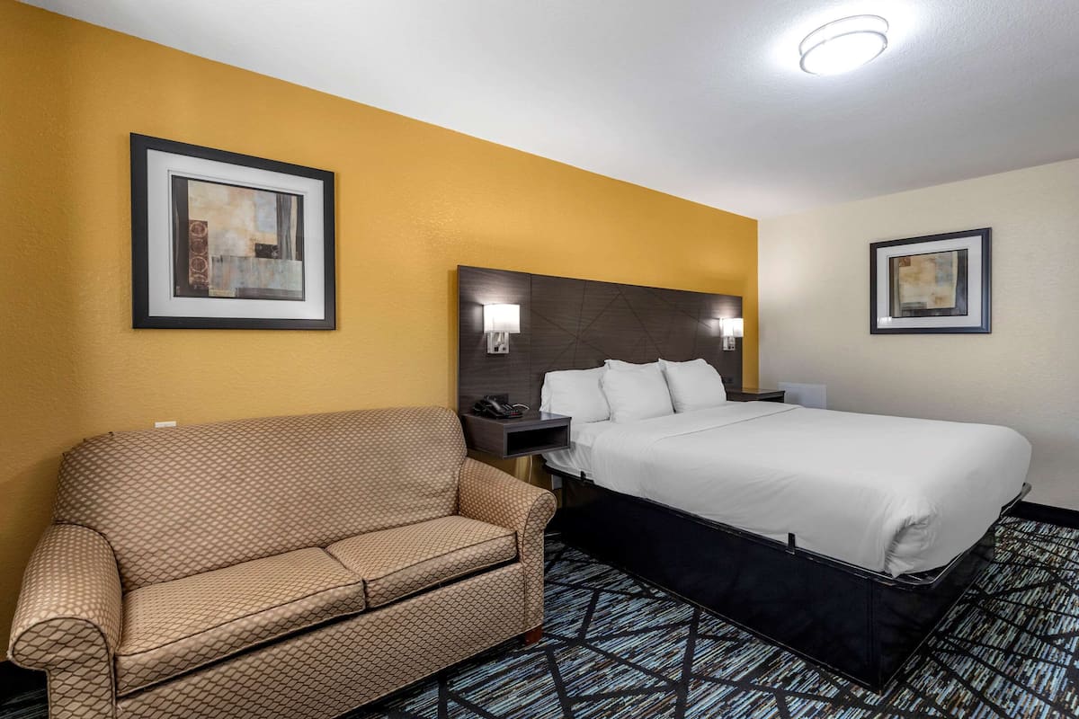 Quarto de hotel com uma cama, um sofá e duas luminárias fixadas na parede.