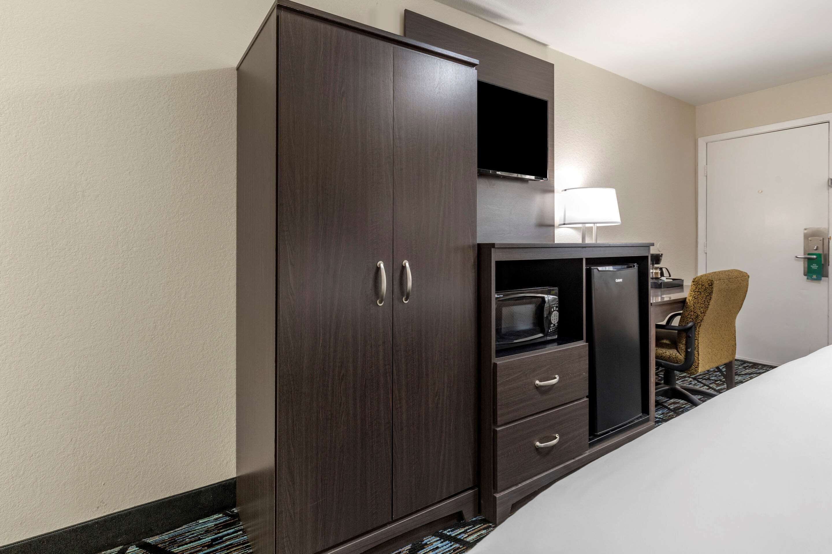 Habitación de hotel con un armario grande, televisión de pantalla plana, microondas y una silla.