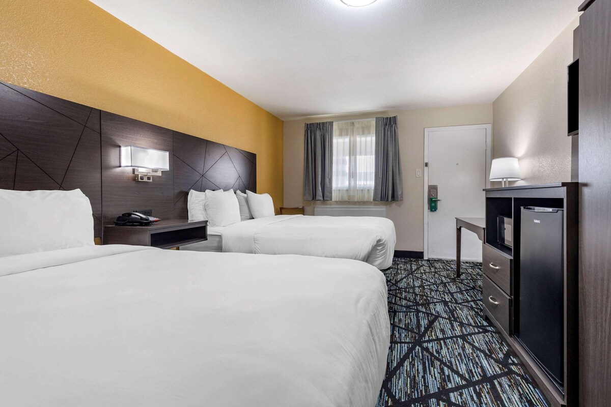 A hotel room with two beds, a desk with a telephone, a minibar, and a television.