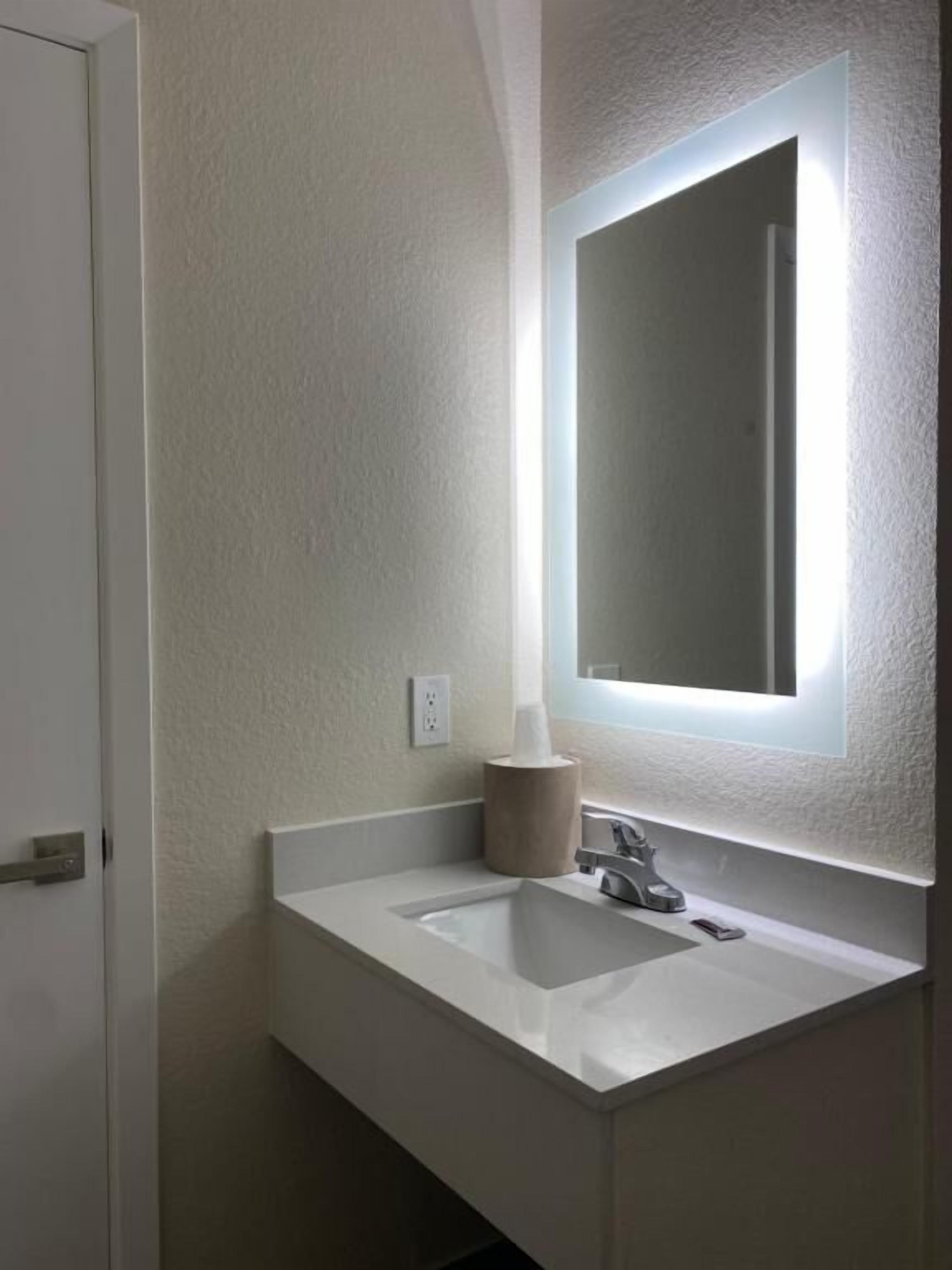 Un baño con lavamanos blanco, espejo y dispensador de pañuelos.
