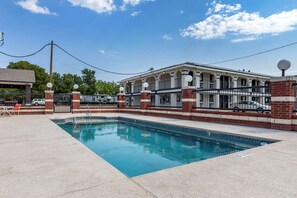 A swimming pool area with a brick building, a covered seating area, and a fenced pool.