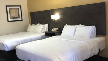 A hotel room with two single beds, a nightstand with a phone, a framed picture on the wall, and a patterned carpet.