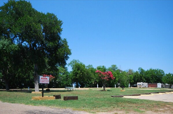 Entrada a un parque para vehículos recreativos, con un letrero, mesas de picnic y un estacionamiento.
