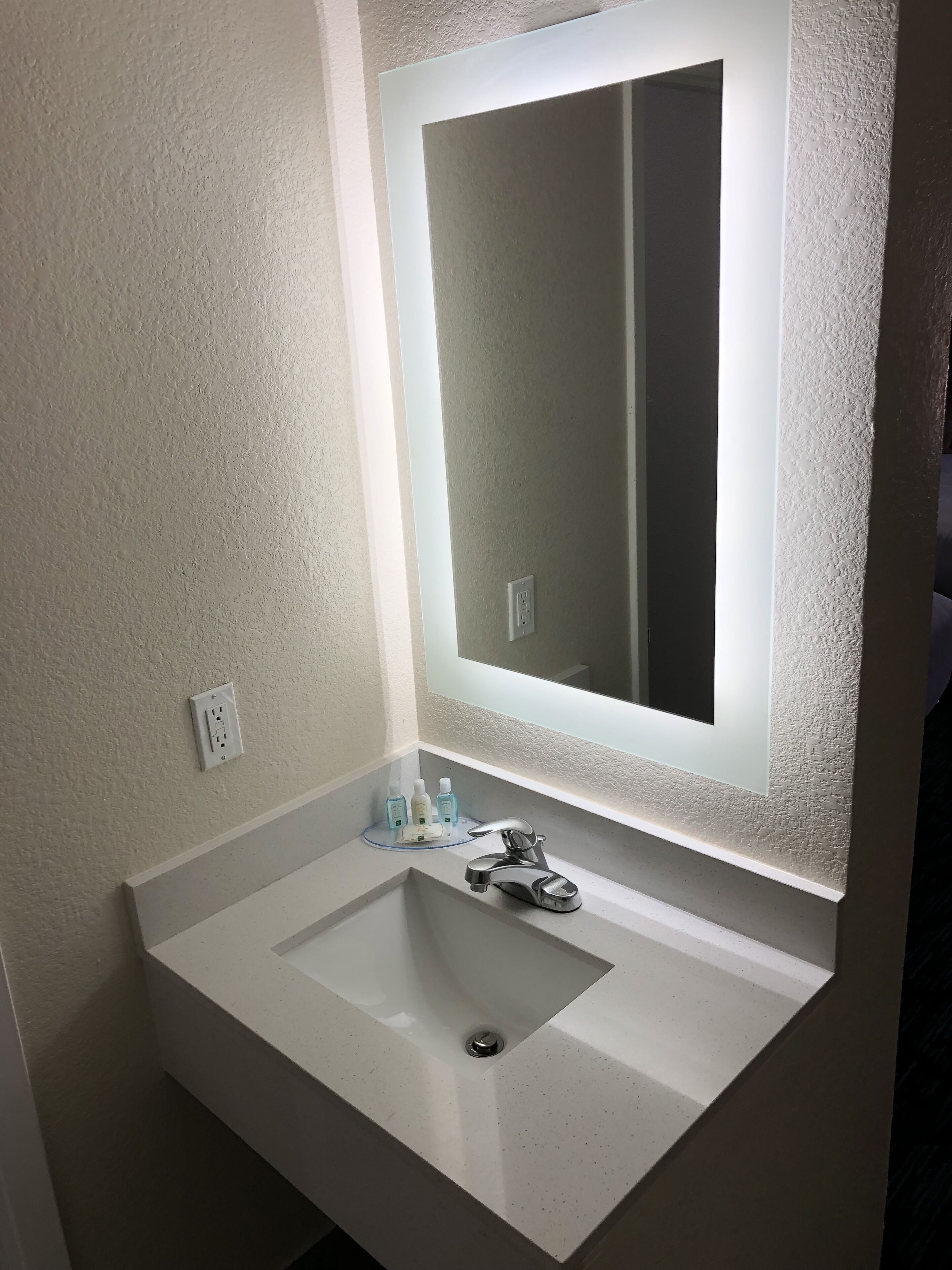 A bathroom with a white sink, a mirror with a light, and a few toiletries on the counter.