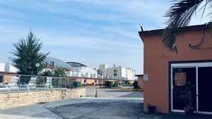 A parking area with a building entrance, a stone wall, and a palm tree. - Hotel Rio Inn (Boca del Río)
