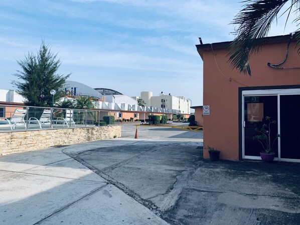 A parking area with a building entrance, a stone wall, and a palm tree.