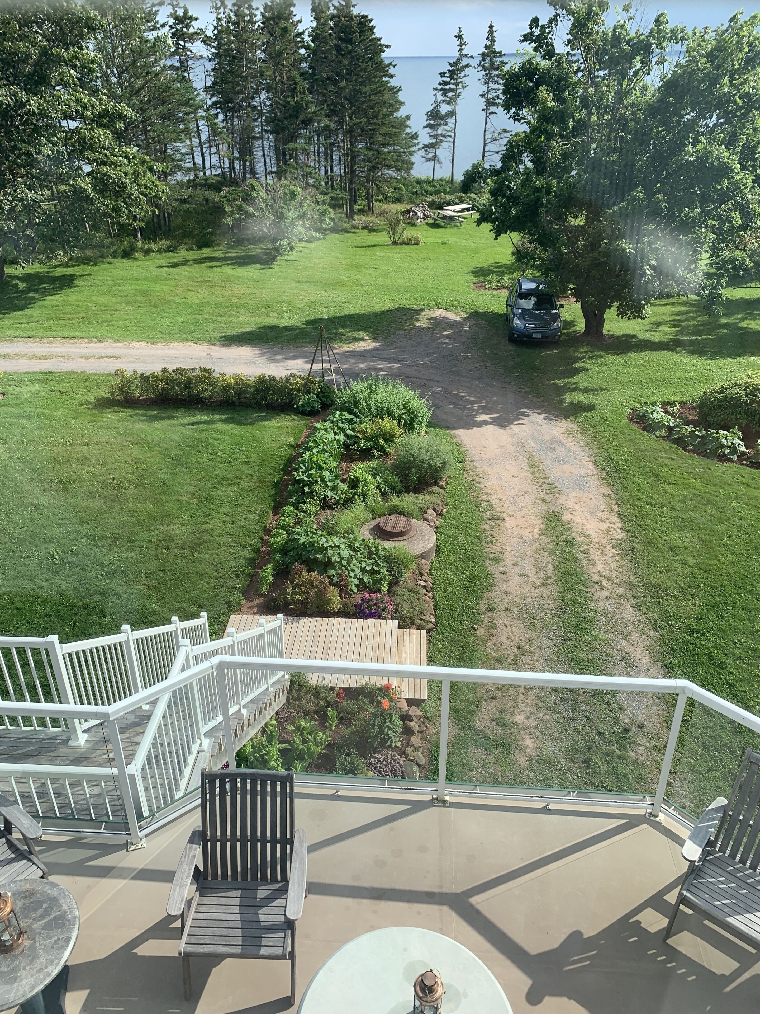 A deck with outdoor furniture, a garden path, and a view of a forest and water body.