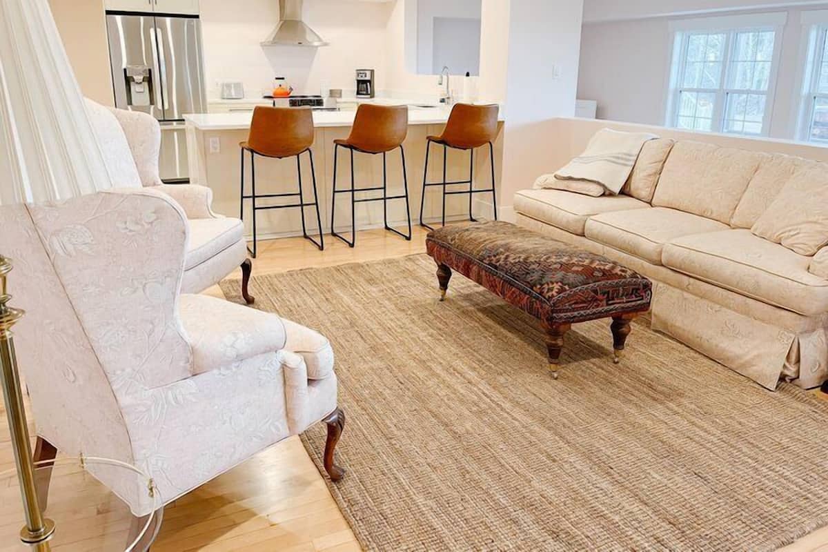 A living room with a sofa, armchair, ottoman, and bar stools.