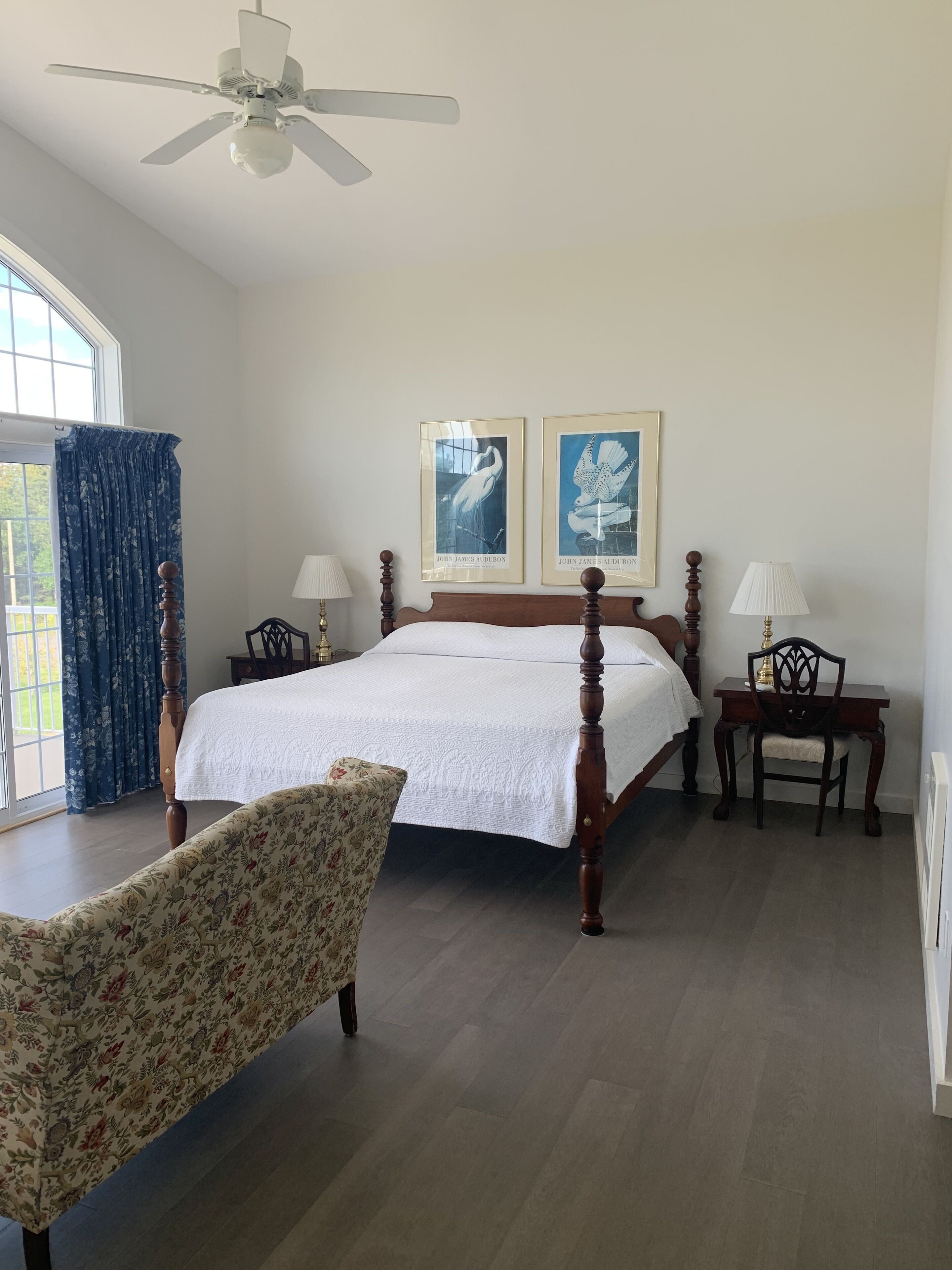 Une chambre à coucher avec un grand lit, deux tables de chevet avec des lampes, une chaise et deux tableaux encadrés accrochés au mur.