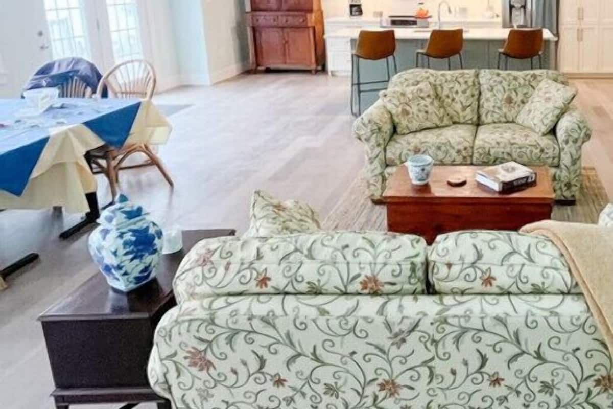 A spacious living area with a sofa, a coffee table, and a dining table set with chairs. There is a kitchen area with cabinets and a countertop.