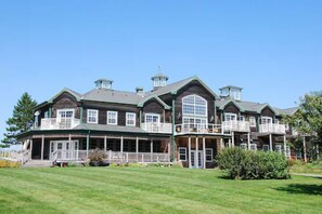 A large, multi-story building with a prominent balcony on the second floor, a covered porch area, and a well-maintained lawn in front.