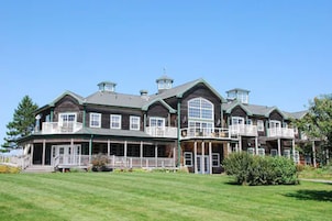 A large, multi-story building with a prominent balcony on the second floor, a covered porch area, and a well-maintained lawn in front.