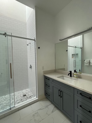 A modern bathroom with a glass shower enclosure, a large mirror, and grey cabinetry.