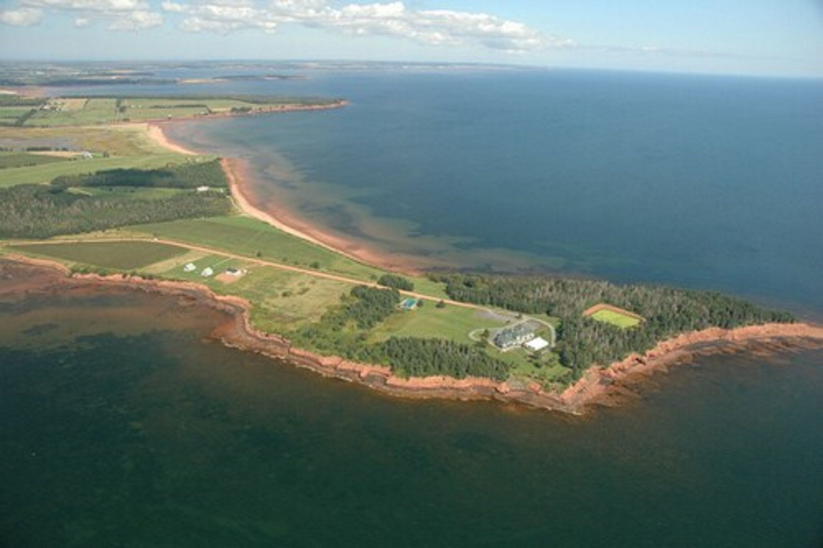 An aerial view of a coastal area with a beach, green fields, and a small building.