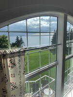 A bay window with a view of a grassy area and a body of water.