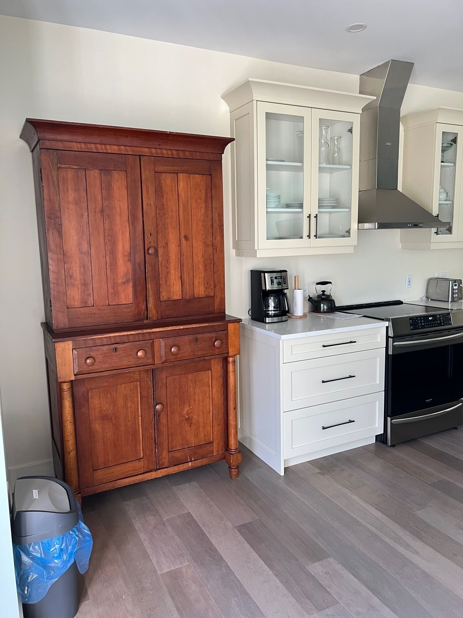 A kitchen with wooden cabinets, a white countertop, a stainless steel range hood, and a trash bin.