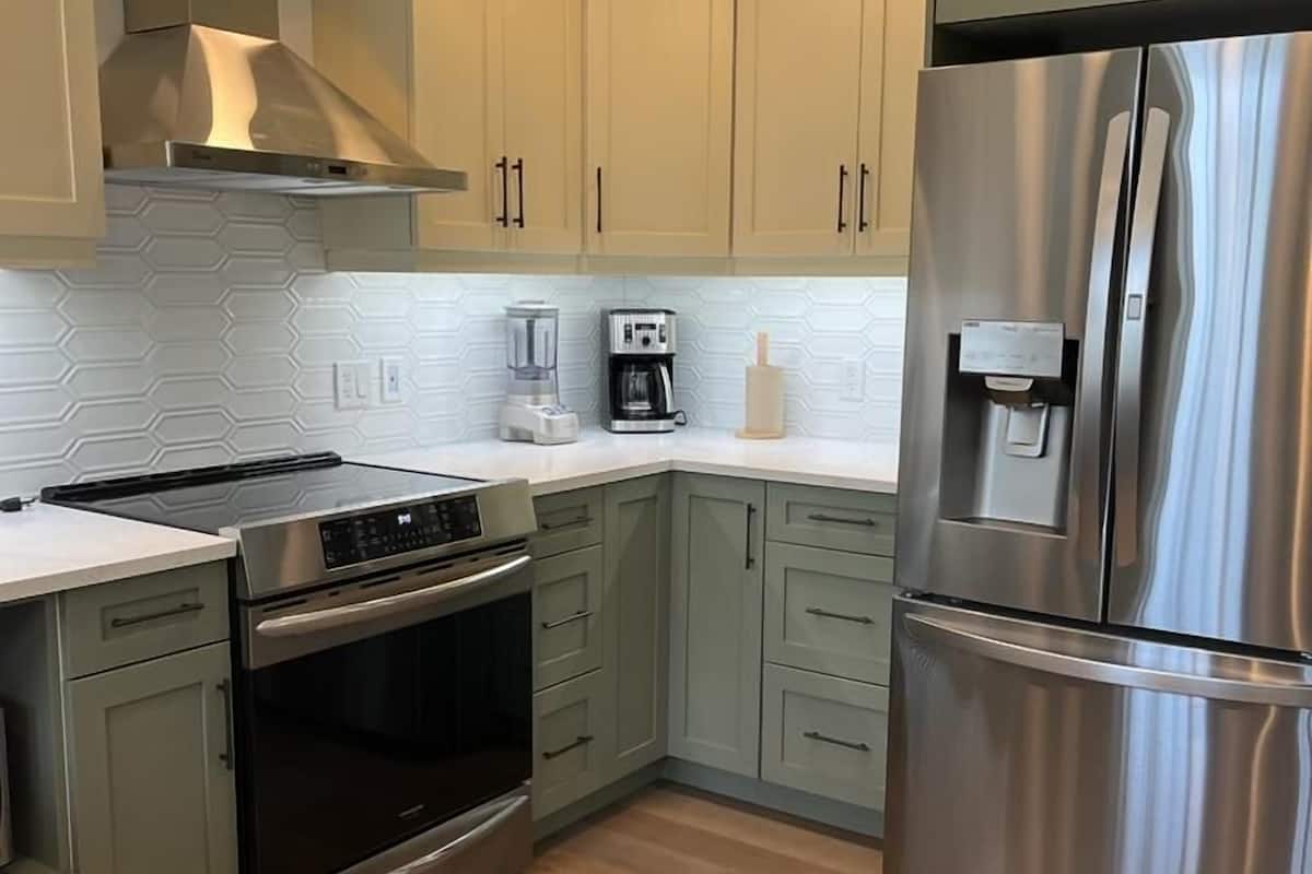 A modern kitchen with light green cabinets, stainless steel appliances, and a central island.