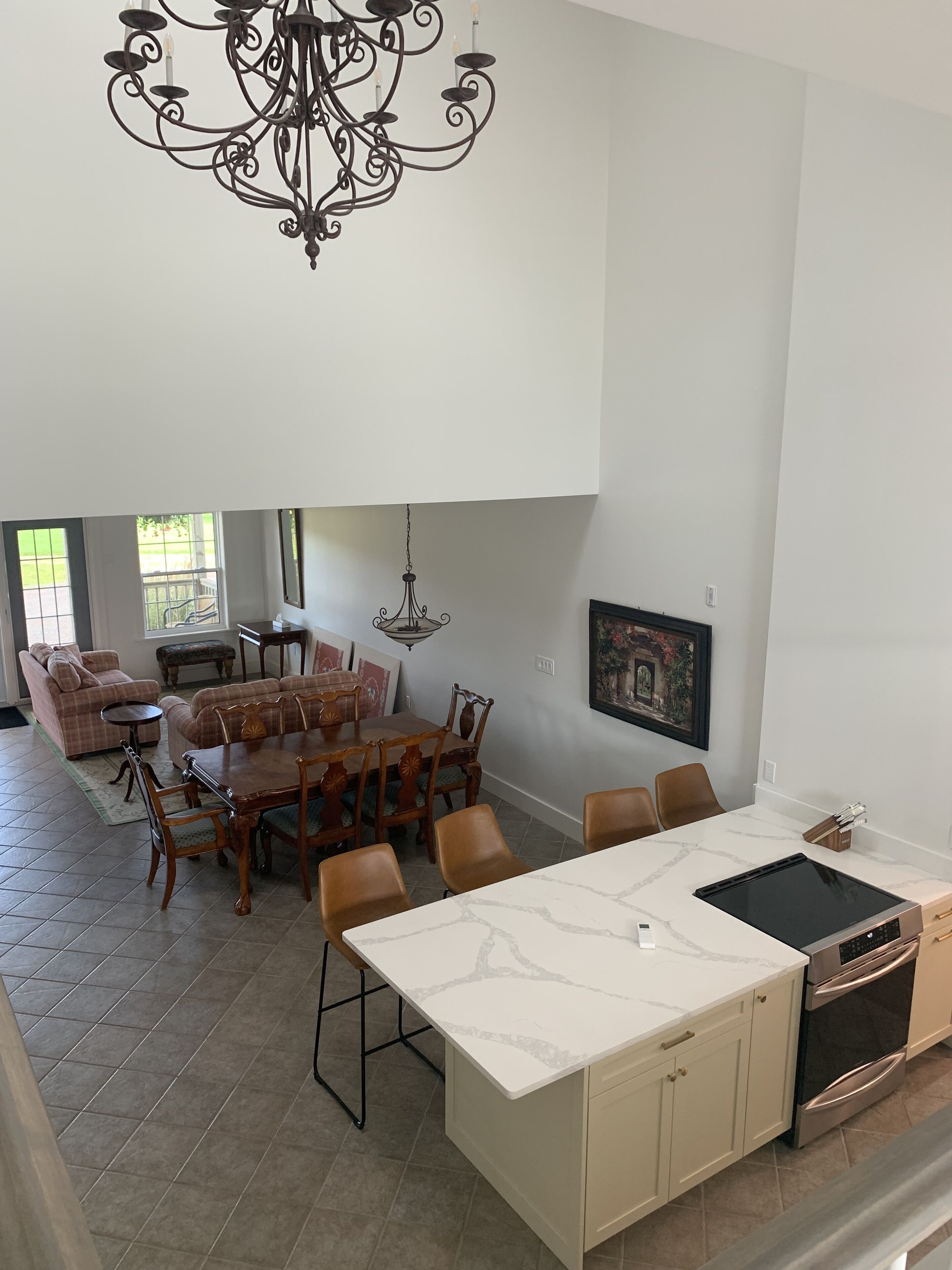 Una cocina amplia con encimera de mármol, una zona de comedor con mesa y sillas de madera, una araña y un ventanal grande.