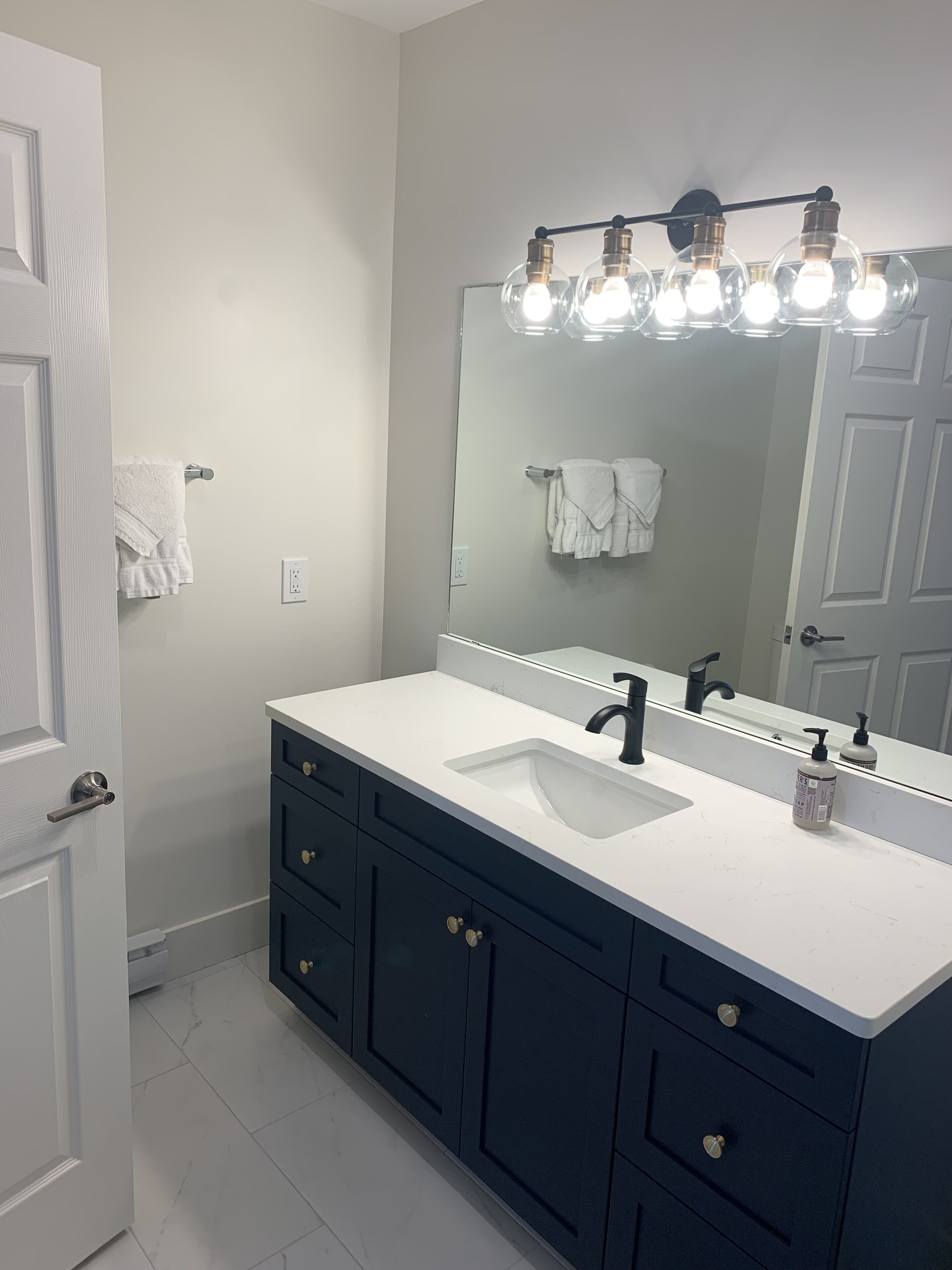 A bathroom with a white sink, dark blue cabinets, and a mirror with lights above.