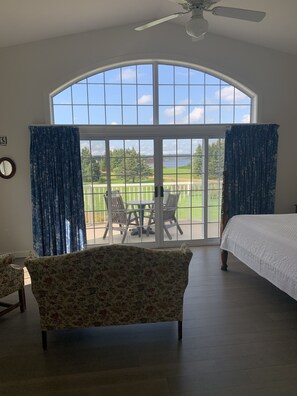 A bedroom with a large window, a ceiling fan, a bed, and a chair.