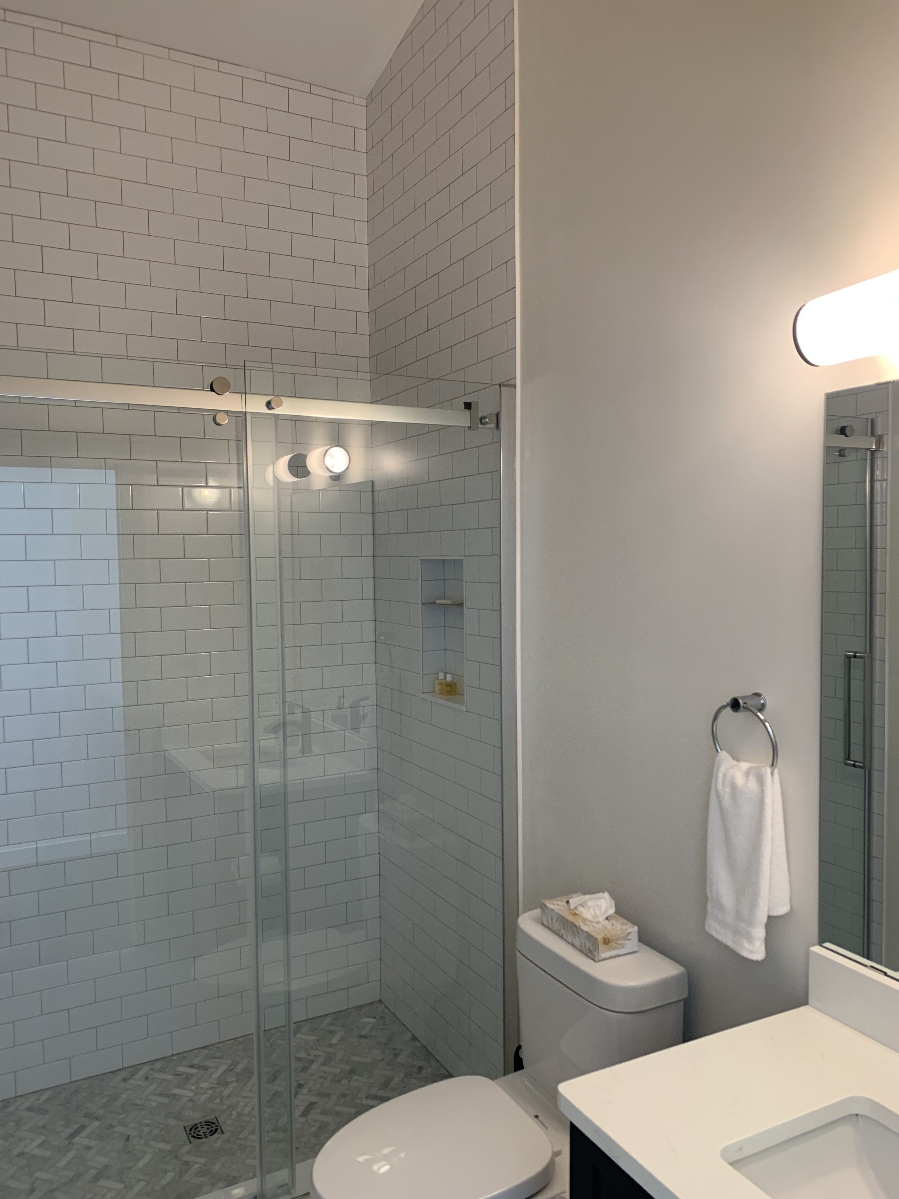 Een moderne badkamer met een douchecabine van glas, witte tegels, een toilet en een wastafel.