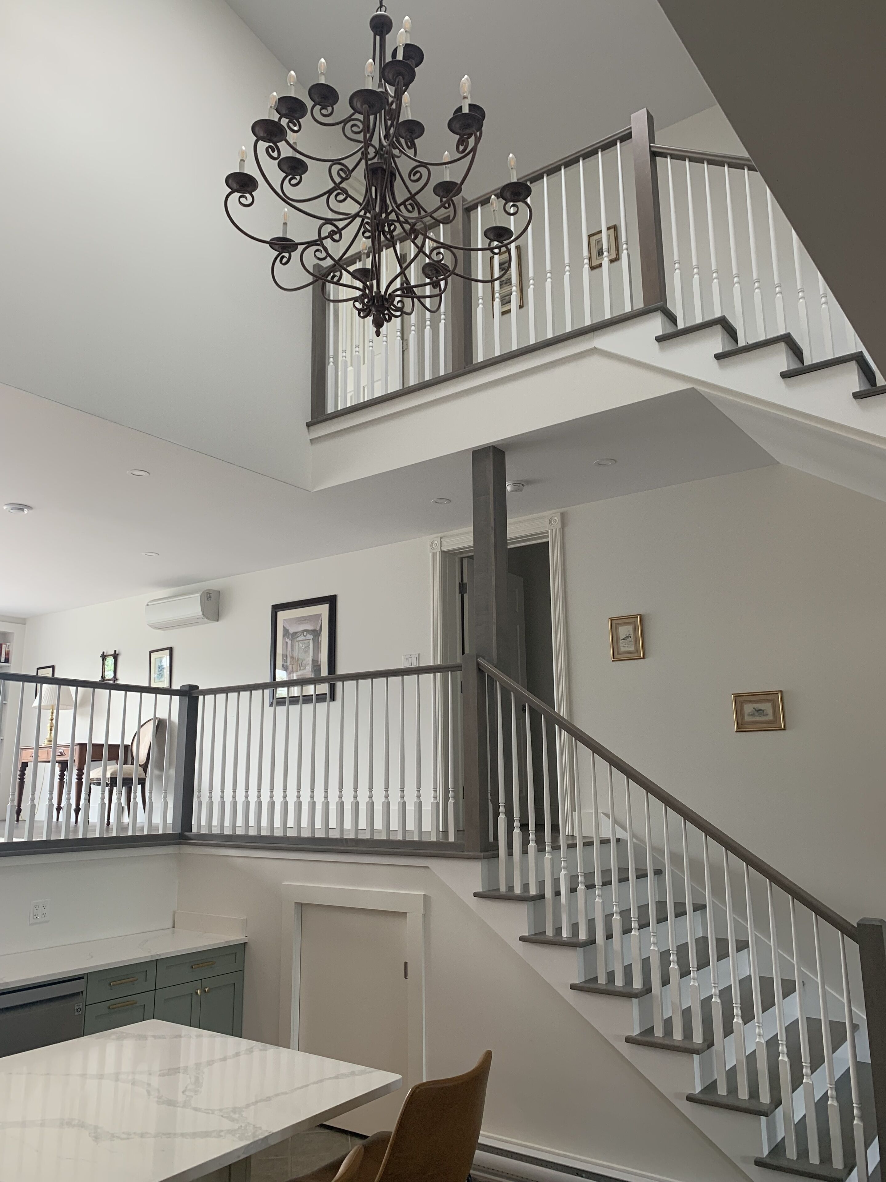 A spacious kitchen with a dining table and chairs, a staircase with white railings, and a chandelier.