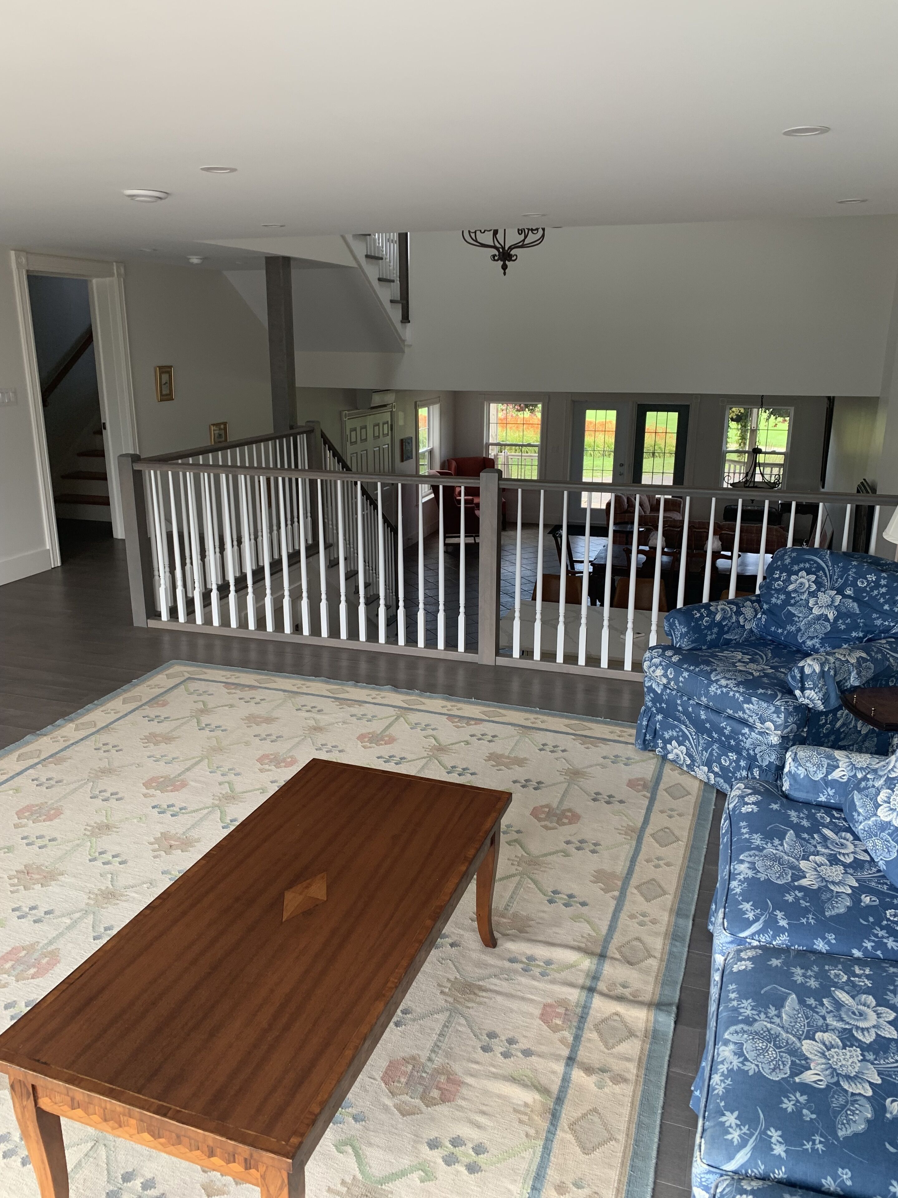 A spacious living room with a wooden coffee table, a blue floral sofa, and a view of a backyard through large windows.