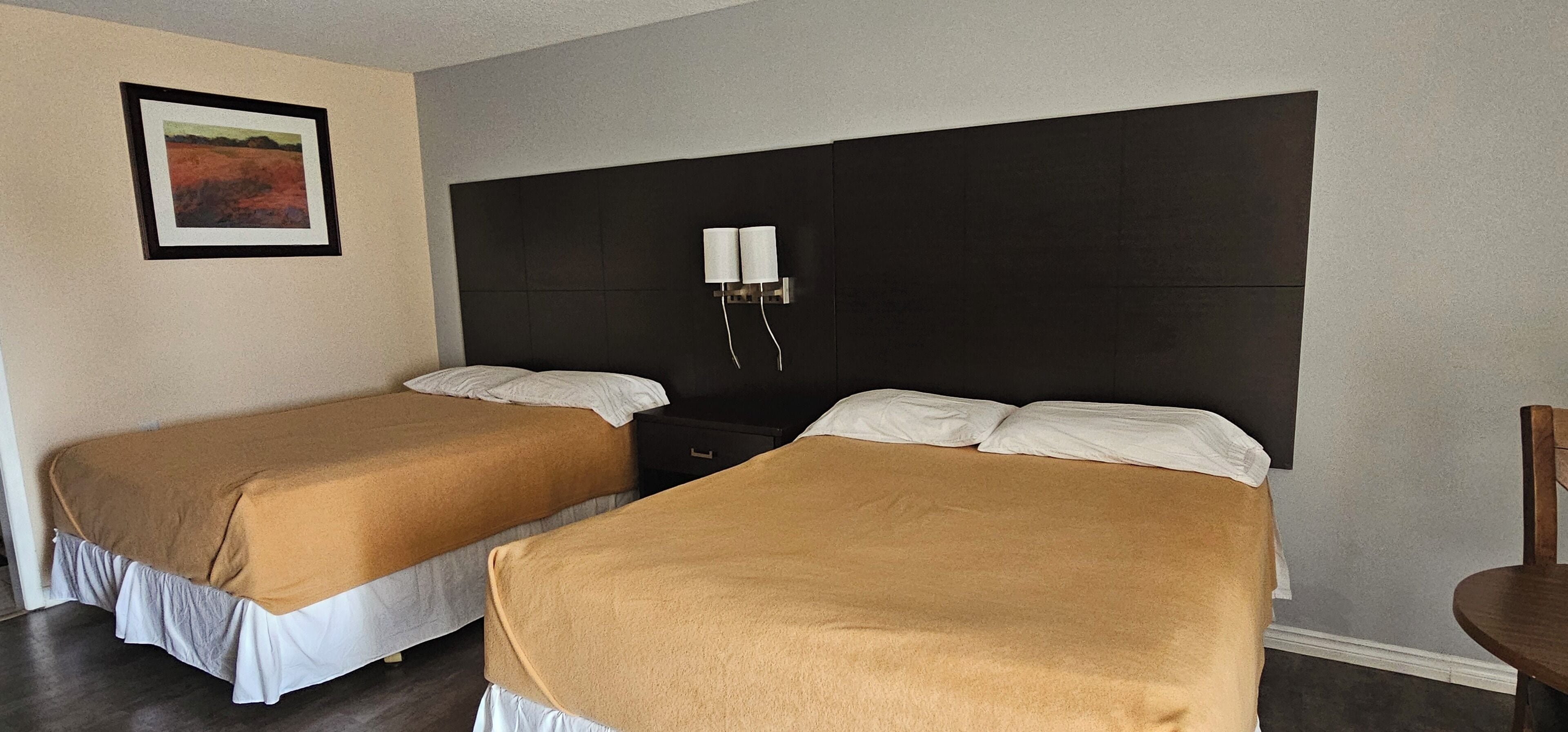 Habitación de hotel con dos camas individuales, un cabecero oscuro, una mesita de noche con lámparas y un cuadro enmarcado en la pared.