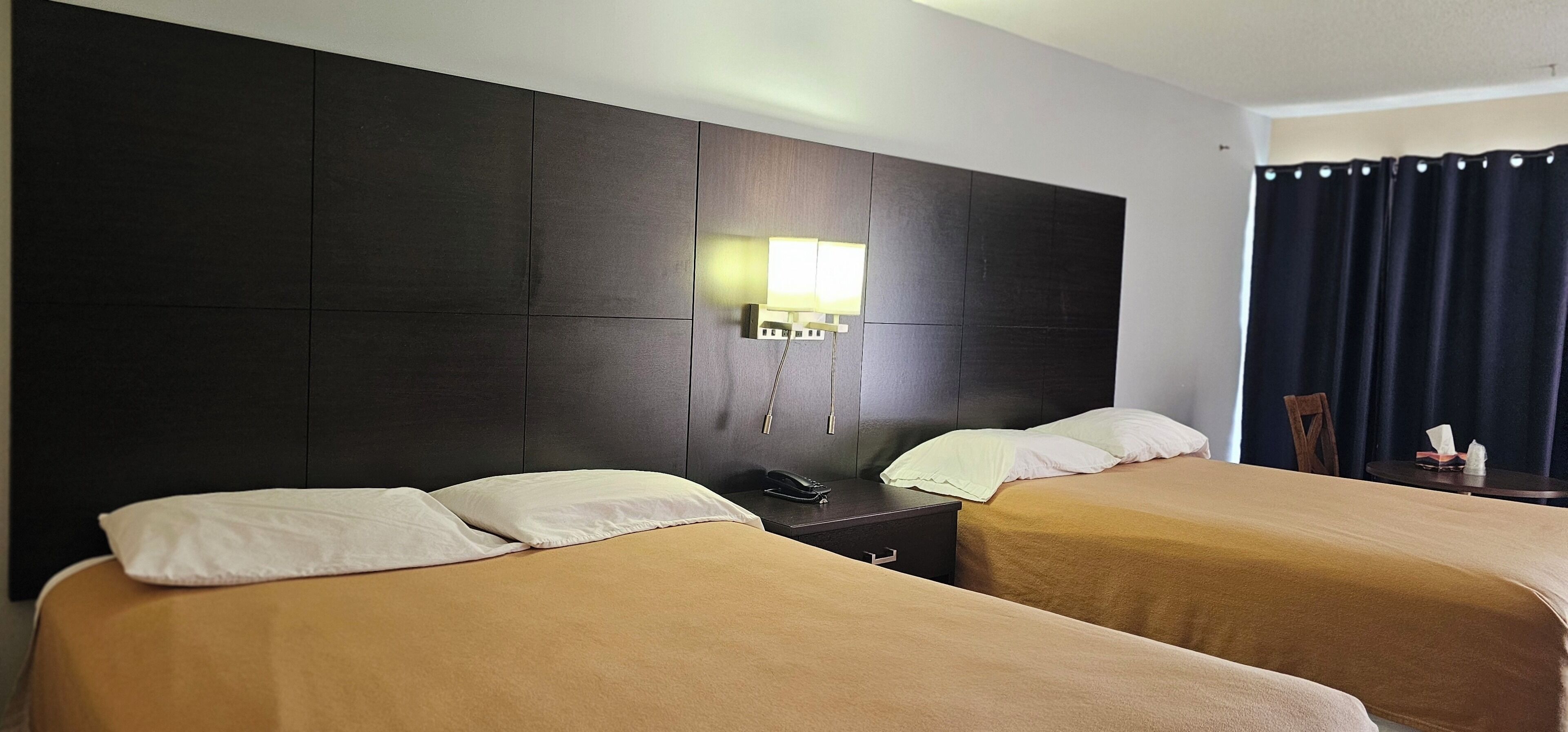 A hotel room with two beds, a nightstand, a lamp, and a window with curtains.