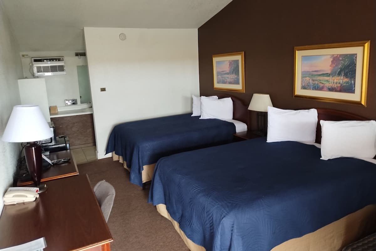 A hotel room with two beds, a desk, a lamp, a phone, and a painting on the wall.