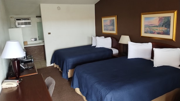 A hotel room with two beds, a desk, a lamp, a phone, and a painting on the wall.